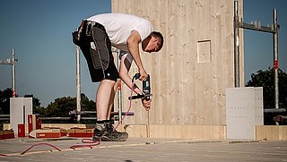 Foto, eine Person in Arbeitskleidung bohrt auf einer Baustelle in den Fußboden.